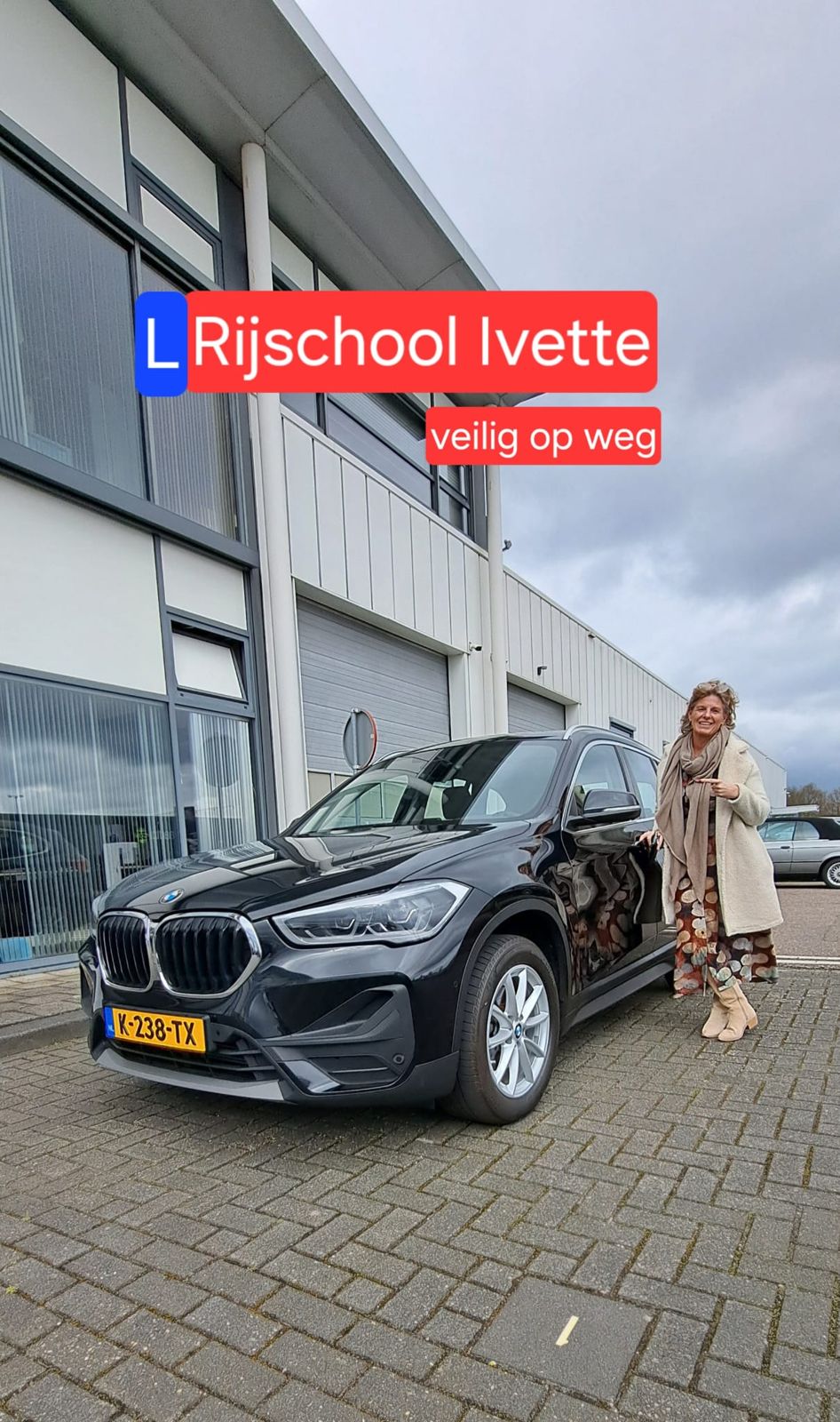 Ivette bij haar zwarte lesauto voor een bedrijfspand, met het logo van Rijschool Ivette