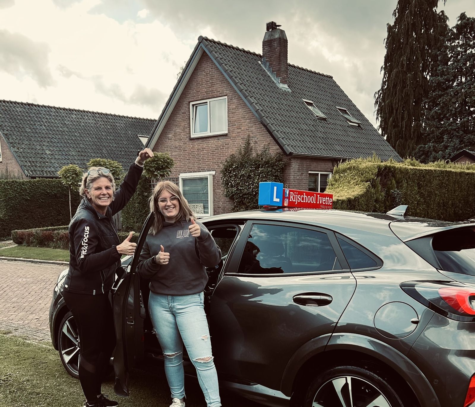 Ivette en een leerling steken hun duim op naast de lesauto van Rijschool Ivette