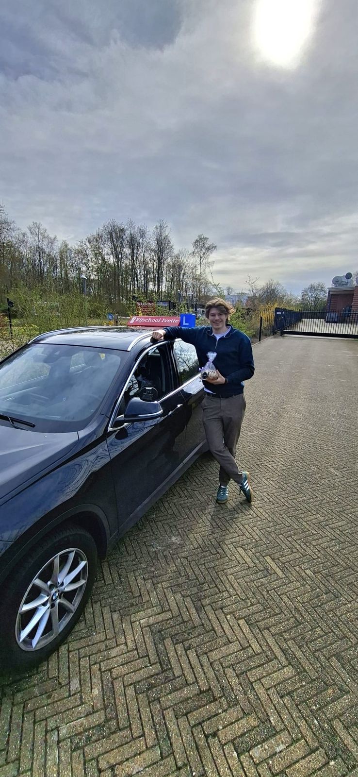 Een geslaagde leerling staat naast de lesauto